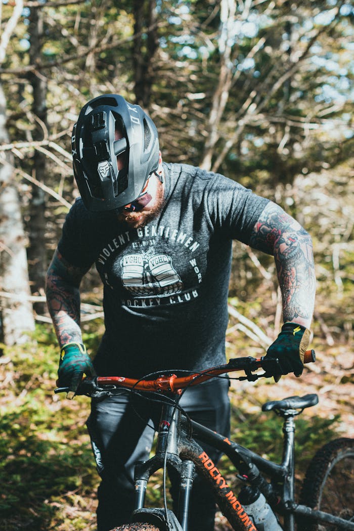 Man with arm tattoos riding a mountain bike through a sunlit forest, showcasing outdoor adventure and fitness.