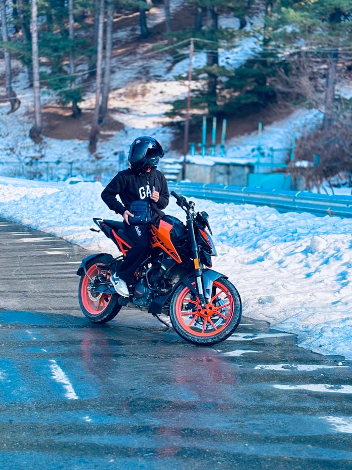 A motorbike rider pauses on a snowy road in a serene forest setting.